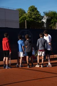 Gruppe Jugendlicher mit Tennisschlägern steht auf einem Sandplatz vor einer Wertetafel und dem Vereinsbanner des SFE 1880