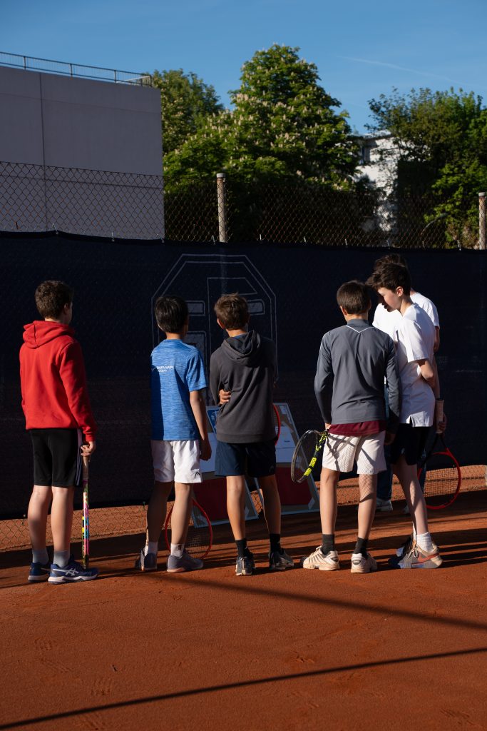 Gruppe Jugendlicher mit Tennisschlägern steht auf einem Sandplatz vor einer Wertetafel und dem Vereinsbanner des SFE 1880