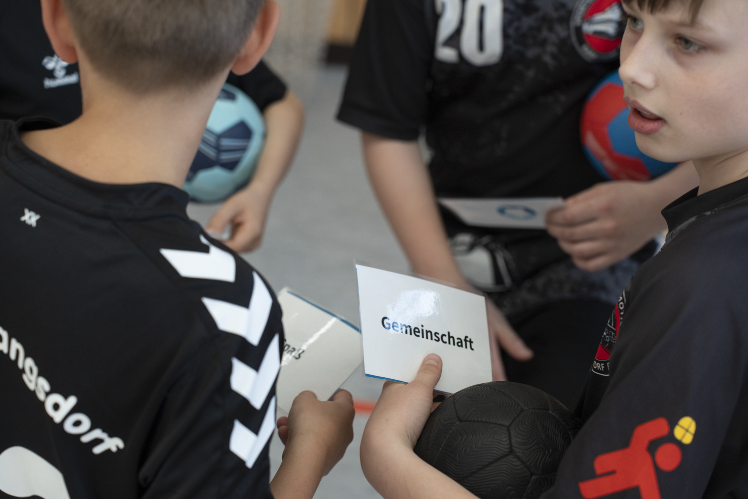 Jungen in Handballtrikots des SV Lokomotive Rangsdorf sitzen im Kreis, einer hält eine Karte mit der Aufschrift „Gemeinschaft“