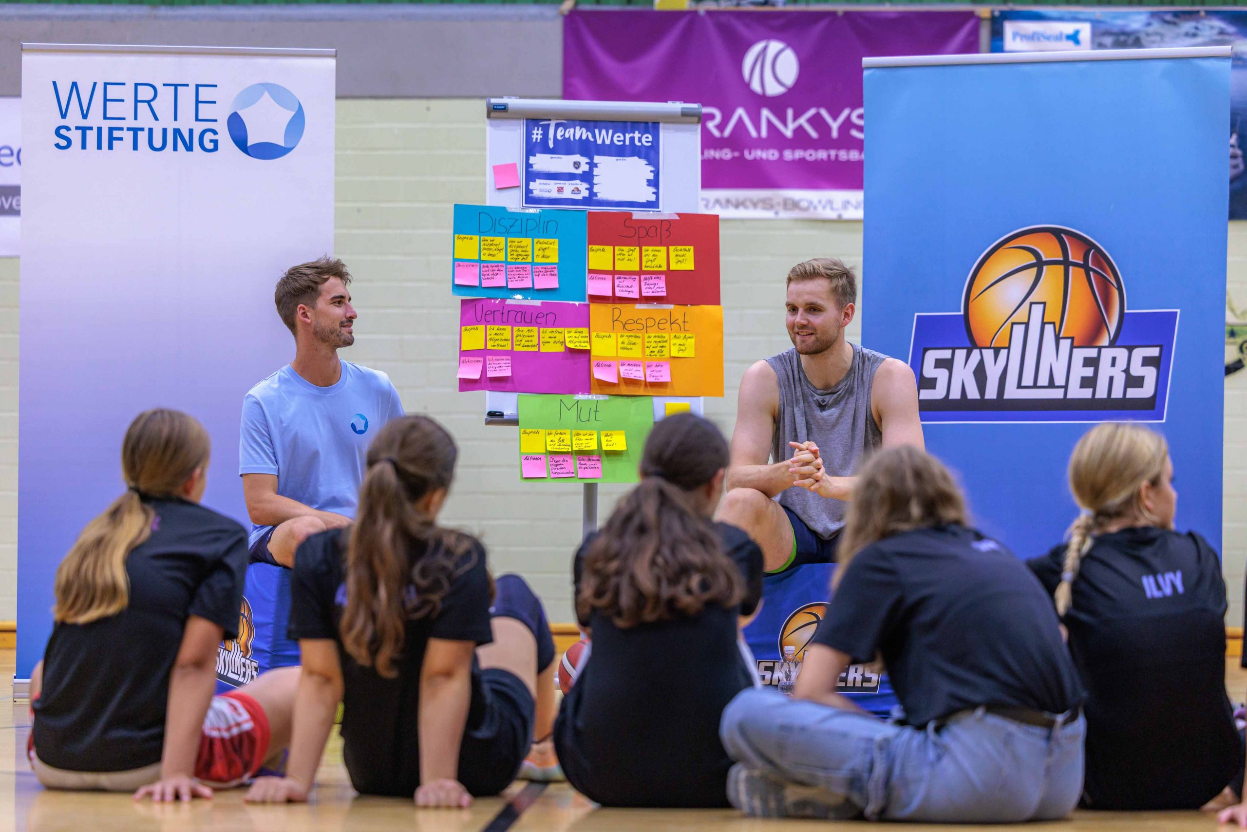 Werte-Coach der Werte-Stiftung gemeinsam mit SKYLINERS-Kapitän Till Pape vor einem Werte-Plakat